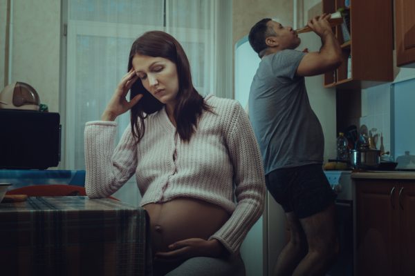 pregnant woman with male partner drinking in the background